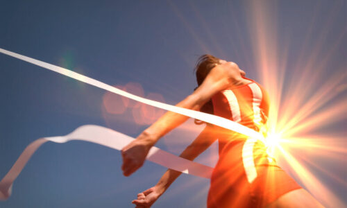 Low,Angle,View,Of,Young,Female,Athlete,Crossing,Finish,Line